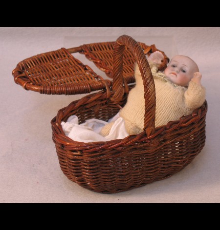 An early 20th Century continental bisque headed blue eyed baby in a basket